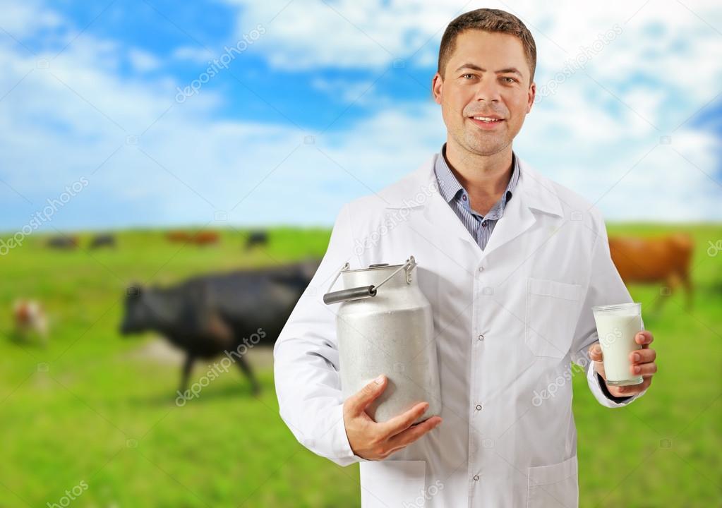 Professional expert with can and glass of milk on blurred cow pasture background. Dairy product concept.