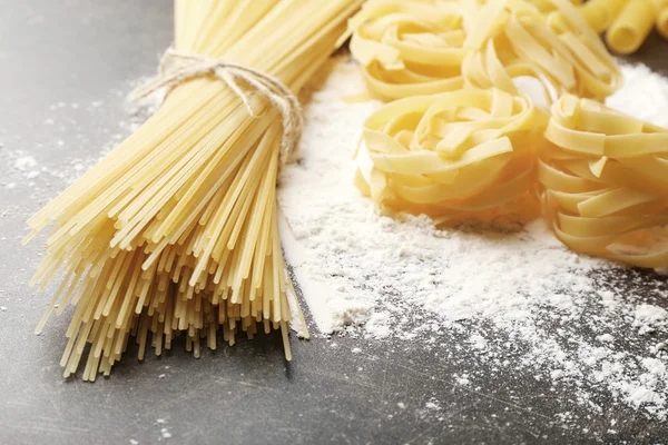 Verschillende droge pasta met bloem op grijze tafel — Stockfoto