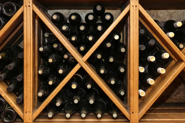 Bottles with wine on wooden shelves in cellar — Stock Photo, Image