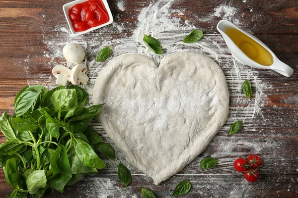 Pizza dough in heart shape with ingredients on table