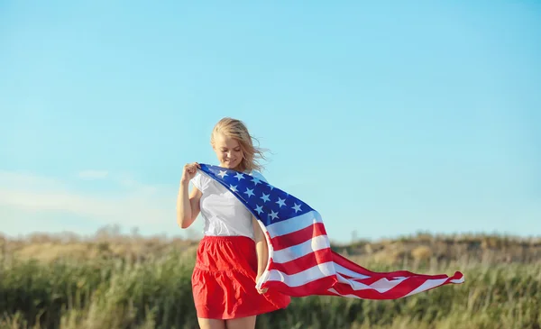 青い空を背景にフィールドでアメリカの国旗を保持している若い女性 — ストック写真