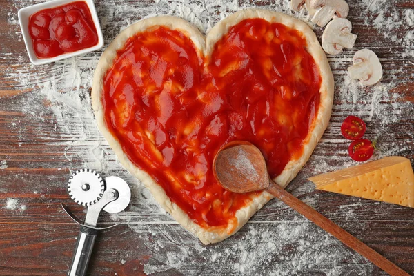 Pizza hamur masada domates sos ile kaplı kalp şeklinde