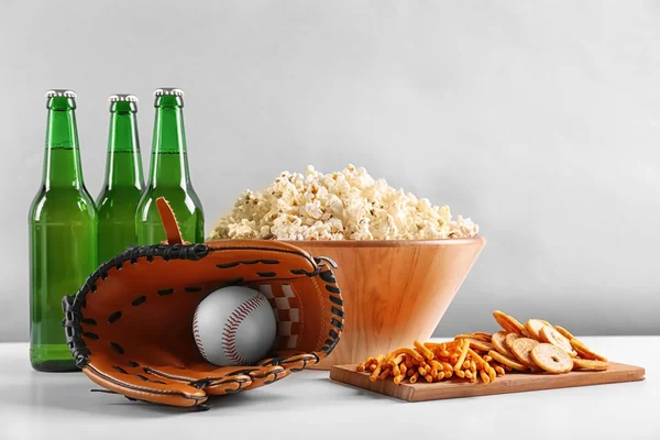 Baseball glove, snacks and bottles of beer on table against light background — Stock Photo, Image