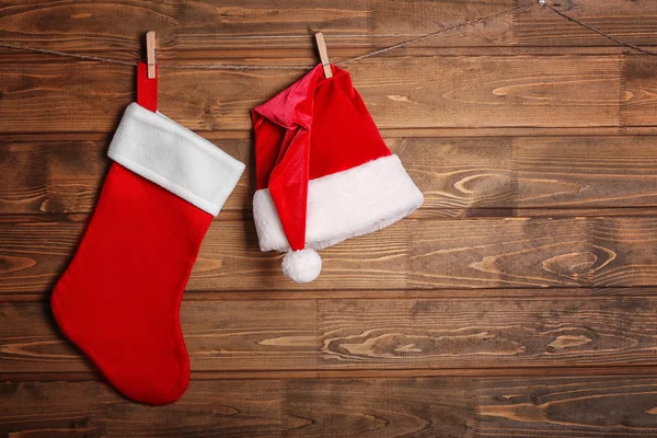 Meia de Natal e chapéu de Papai Noel pendurado contra fundo de madeira — Fotografia de Stock