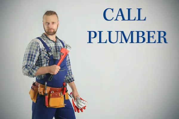 Loodgieter bellen. Knappe loodgieter met pipe wrench en handschoenen aan lichte achtergrond — Stockfoto