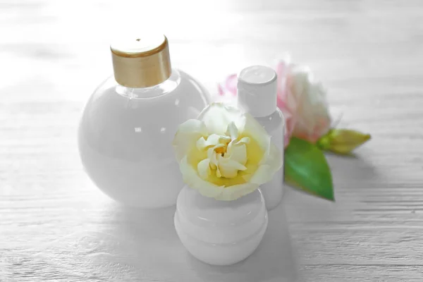 Cosmetic bottles and eustoma flowers on light wooden background — Stock Photo, Image