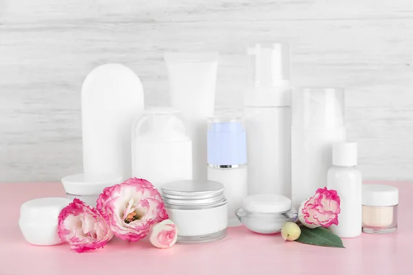 Different cosmetic bottles and flowers on grey wall background — Stock Photo, Image
