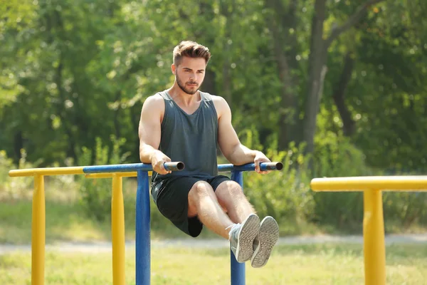 Hombre joven haciendo ejercicios en barra horizontal en el campo de deportes —  Fotos de Stock