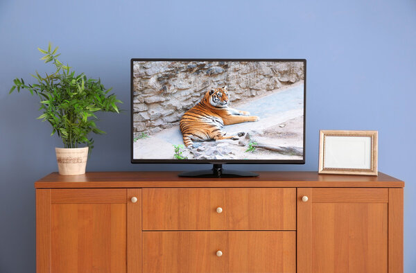 широкоэкранный телевизор на деревянном комоде возле серой стены
