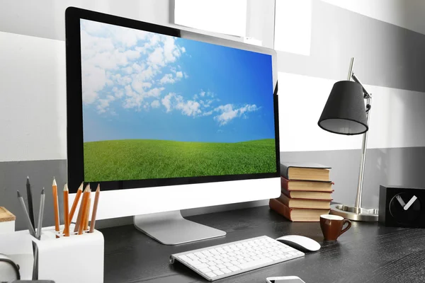Comfortable workplace with modern computer and green spring field on screen — Stock Photo, Image