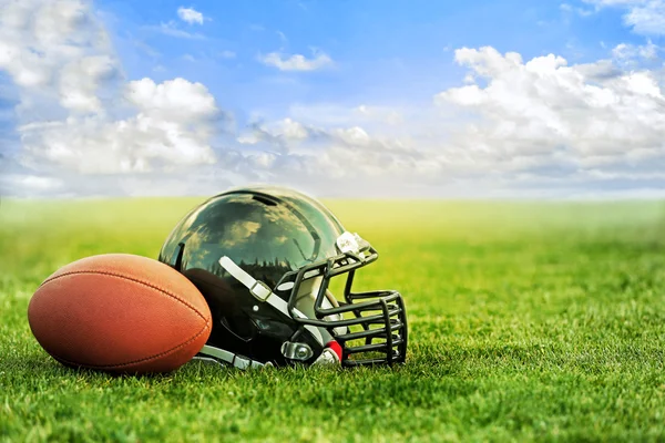Casco de rugby con pelota sobre hierba verde y fondo azul cielo — Foto de Stock