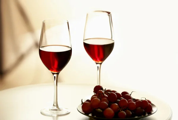Okulary z czerwonego wina i winogron na biały stół — Zdjęcie stockowe