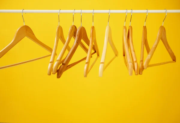 Wooden coat hangers on clothes rail and yellow background — Stock Photo, Image