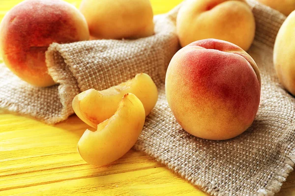 Fresh juicy peaches on bagging and yellow wooden background — Stock Photo, Image