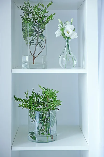 Hermosas flores en jarrones de vidrio en estante blanco — Foto de Stock