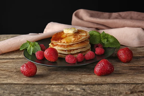Teller mit leckeren Pfannkuchen und Beeren auf Holztisch — Stockfoto