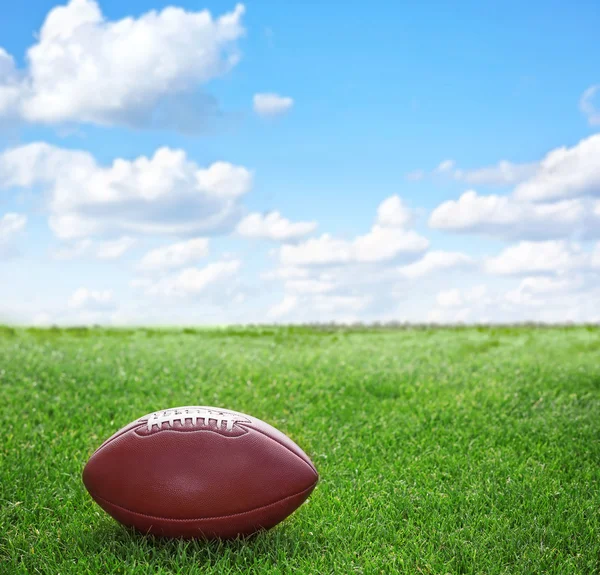 American football ball on green grass and blue sky background — Stock Photo, Image