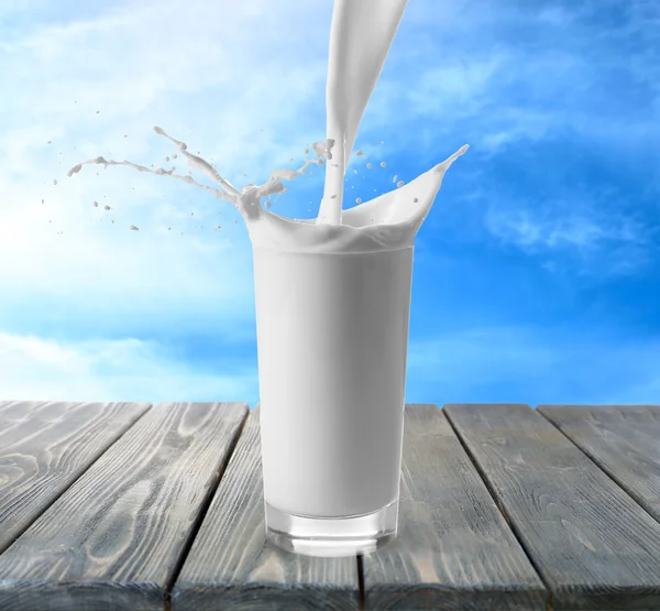 Pouring milk in glass on wooden table with sky background — Stock Photo, Image