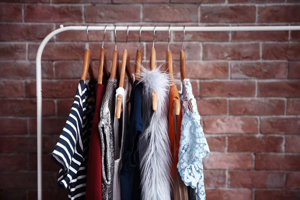 Hangers with different female clothes on brick wall background — Stock Photo, Image