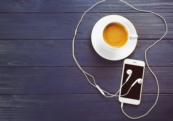 Fones de ouvido, telefone celular e xícara de café em fundo de madeira azul — Fotografia de Stock