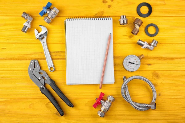 Notebook and plumber tools on yellow wooden background — Stock Photo, Image