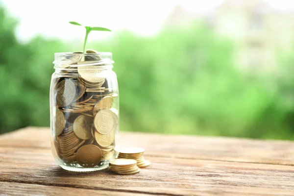 Glas mit Münzen und grüner Pflanze auf Holztisch, Finanzinvestitionskonzept — Stockfoto