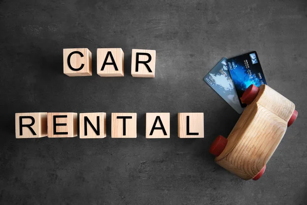 Cubes with words CAR RENTAL and wooden toy on grey background, top view — Stock Photo, Image