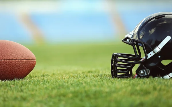 Capacete de rugby com bola no campo — Fotografia de Stock