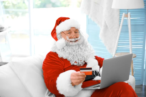 圣诞老人与信用卡和电脑放在家里的沙发上 — 图库照片