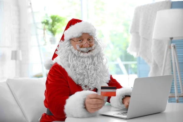 Santa Claus con tarjeta de crédito y portátil en casa — Foto de Stock