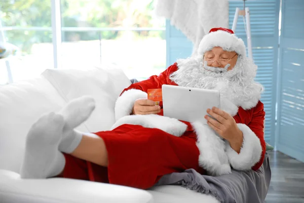 Santa Claus con tarjeta de crédito y tableta en el sofá en casa — Foto de Stock