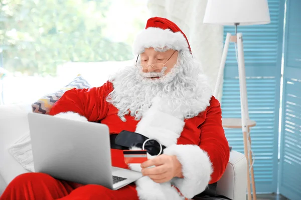 Święty Mikołaj z karty kredytowej i laptop na kanapie w domu — Zdjęcie stockowe