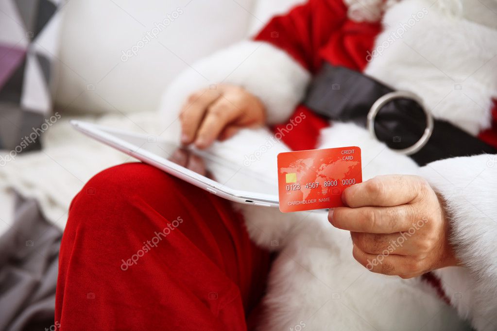 Santa Claus with credit card and tablet on couch at home