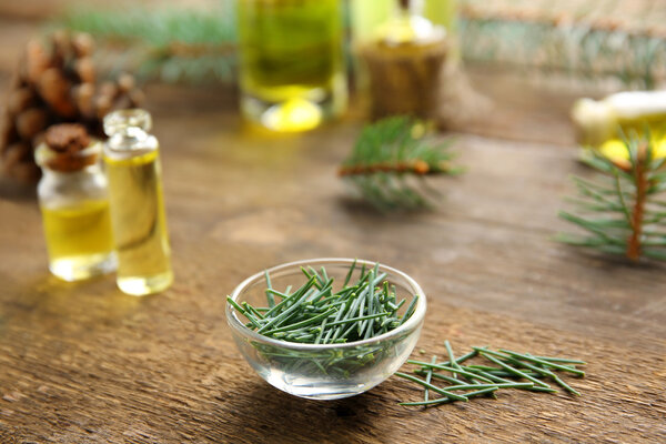Glass bowl with fir tree needles on wooden background, close up view