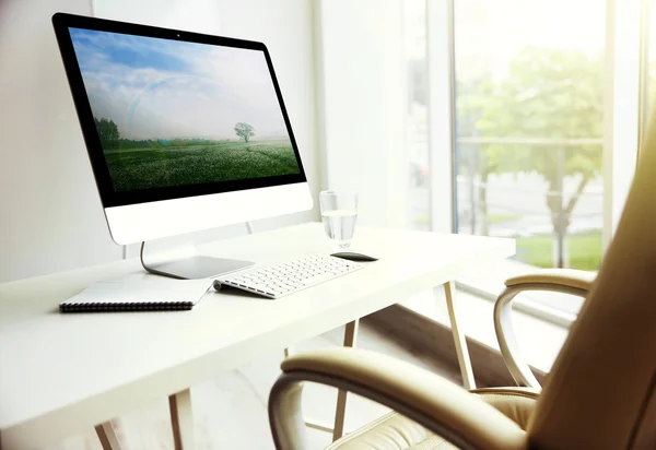 Stylish workplace with modern compute and summer landscape on screen in office
