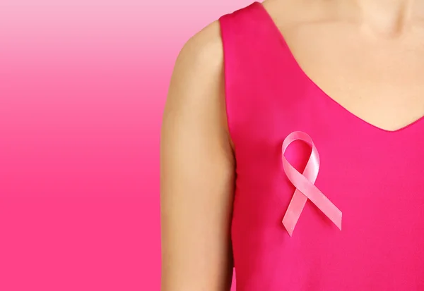 Woman with pink ribbon on chest against color background. Oncology and breast cancer concept. — Stock Photo, Image