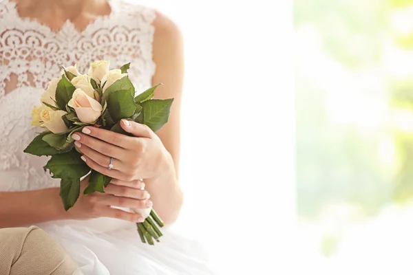 Brud i vackra klänning med bröllop bukett sitter på soffa — Stockfoto
