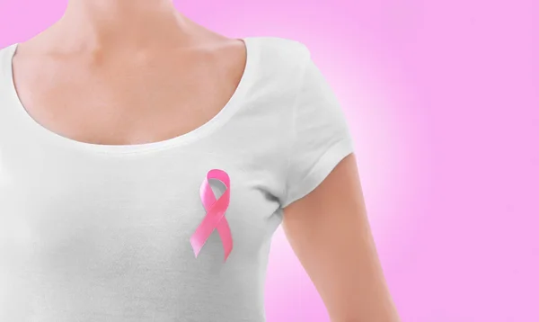 Woman with pink ribbon on chest against color background. Oncology and breast cancer concept. — Stock Photo, Image