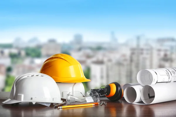 Construction concept. Architect equipment: helmets, blueprint and pencil on the table and view of city — Stock fotografie