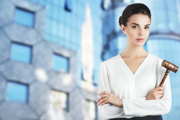 Beautiful woman with judge gavel on blurred city building background. Justice concept. — Stock fotografie
