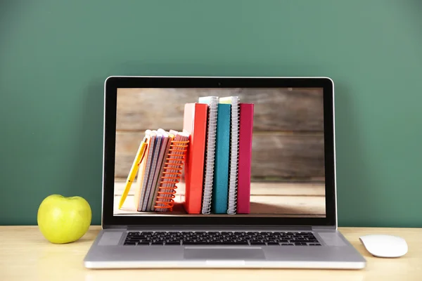 Laptop with stationery wallpaper on screen against chalkboard. School teacher concept. — Stock fotografie