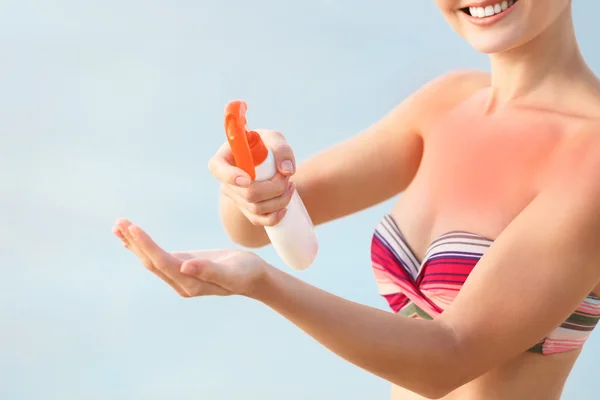 Young woman with red skin holding sun protective cream on the beach — Stock Photo, Image