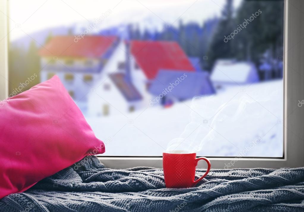 Cup of hot drink on the windowsill in winter landscape background