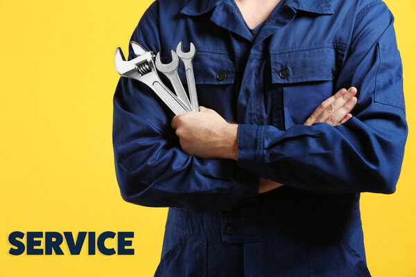 Mechanic with crossed arms and wrench standing on yellow background