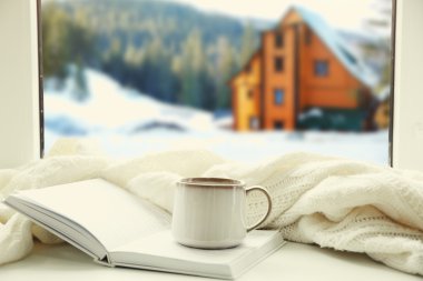 Fincan sıcak içecek ve pencere kış manzara arka planda kitap