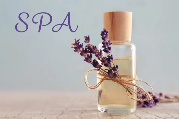 Glass bottle of essential oil on table, closeup. Word SPA on blurred background. — Stock Photo, Image