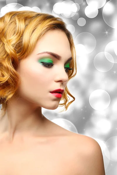 Beautiful girl with colorful makeup and hairstyle on shiny blurred background — Stockfoto