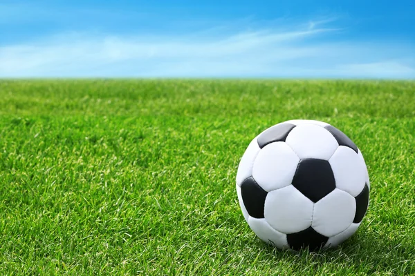 Soccer ball on green grass and blue sky background — Stock Photo, Image