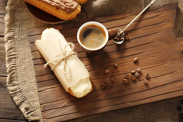 おいしいエクレアと木製の背景のコーヒー カップ — ストック写真