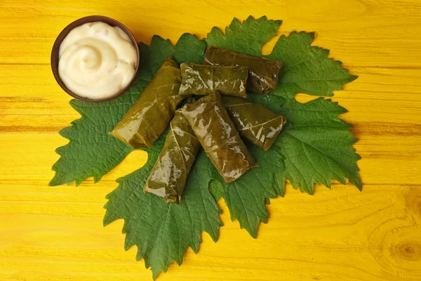 Relleno sabroso Dolma con salsa sobre hoja de vid y fondo de madera amarilla —  Fotos de Stock